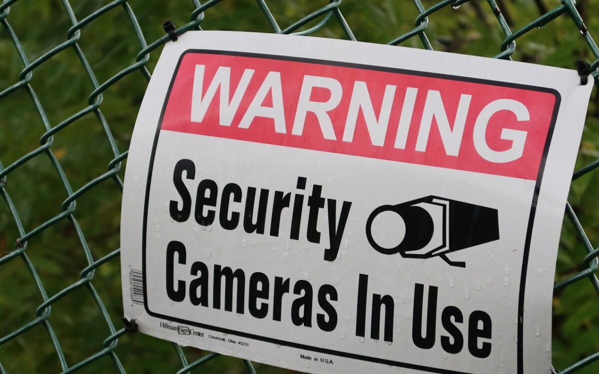 Warning sign reading security cameras in use on a fence